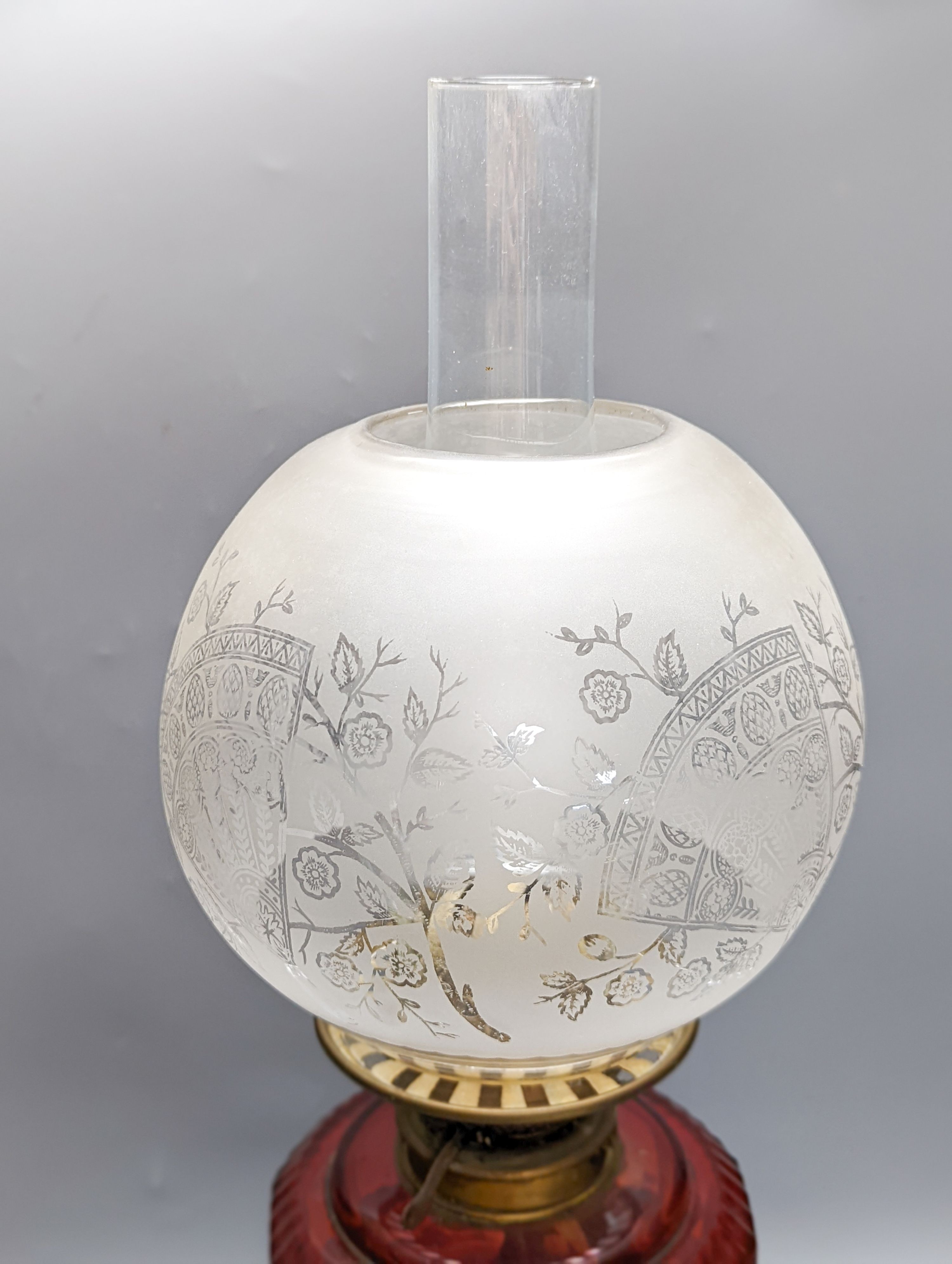 A Victorian brass oil lamp with etched glass shade and cranberry reservoir. 64cm total height